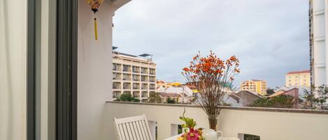 A balcony with a table set for two, a vase with flowers, and a view of buildings in the background.