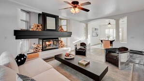 A modern living room with a fireplace, a ceiling fan, and a dining area.