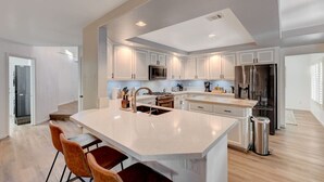 A modern kitchen with white cabinetry, stainless steel appliances, and a central island with bar stools.