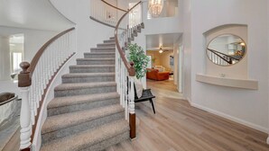 A grand staircase with a wooden handrail, a chandelier, and a large mirror on the wall.