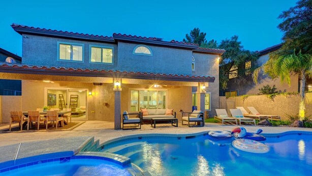 A two-story house with a swimming pool, outdoor seating, and a well-lit patio area.