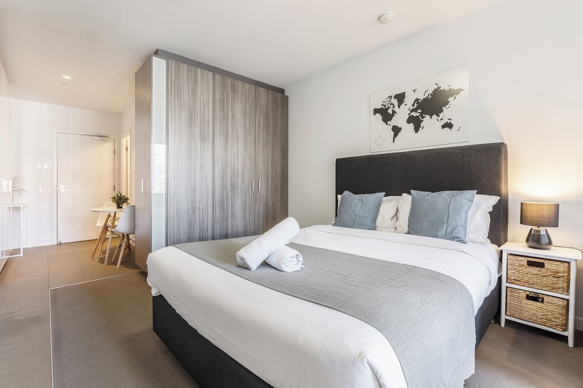 A modern hotel room with a large bed, a bedside table with a lamp, a world map on the wall, and a separate seating area with a table and chairs.