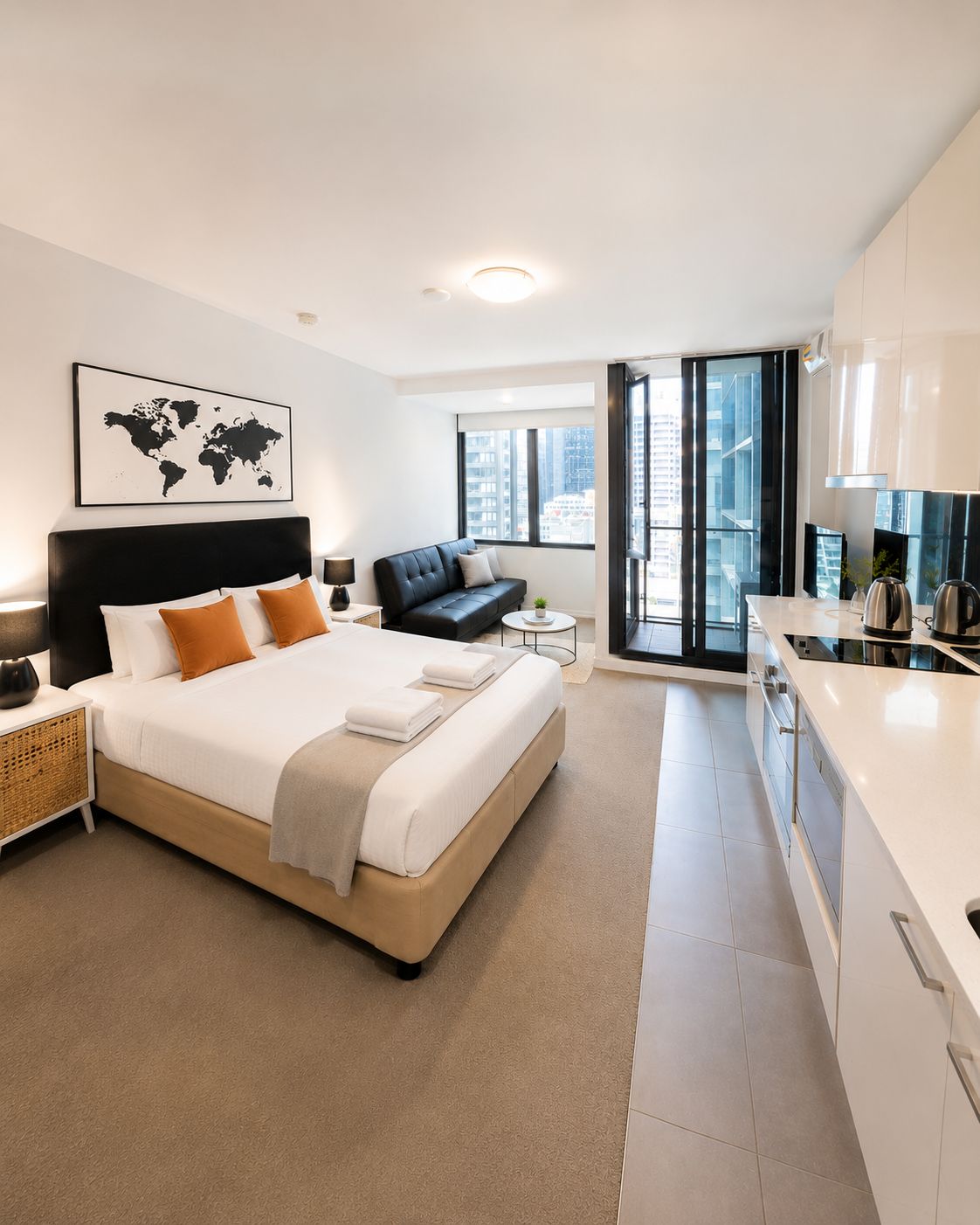 Una habitación de hotel moderna con una cama grande, un sofá, una mesita y una kitchenette.