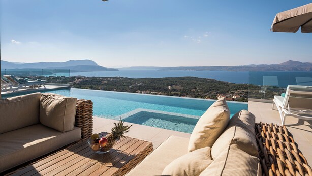 Área de piscina com um sofá, cadeiras de descanso e uma mesa com frutas.
