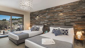 Quarto de hotel moderno com duas camas, parede de pedra, uma janela grande e um candelabro.