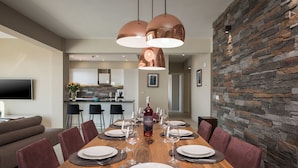 Uma sala de jantar com mesa de madeira posta para seis pessoas, rodeada por cadeiras, com parede de pedra e iluminação pendente.