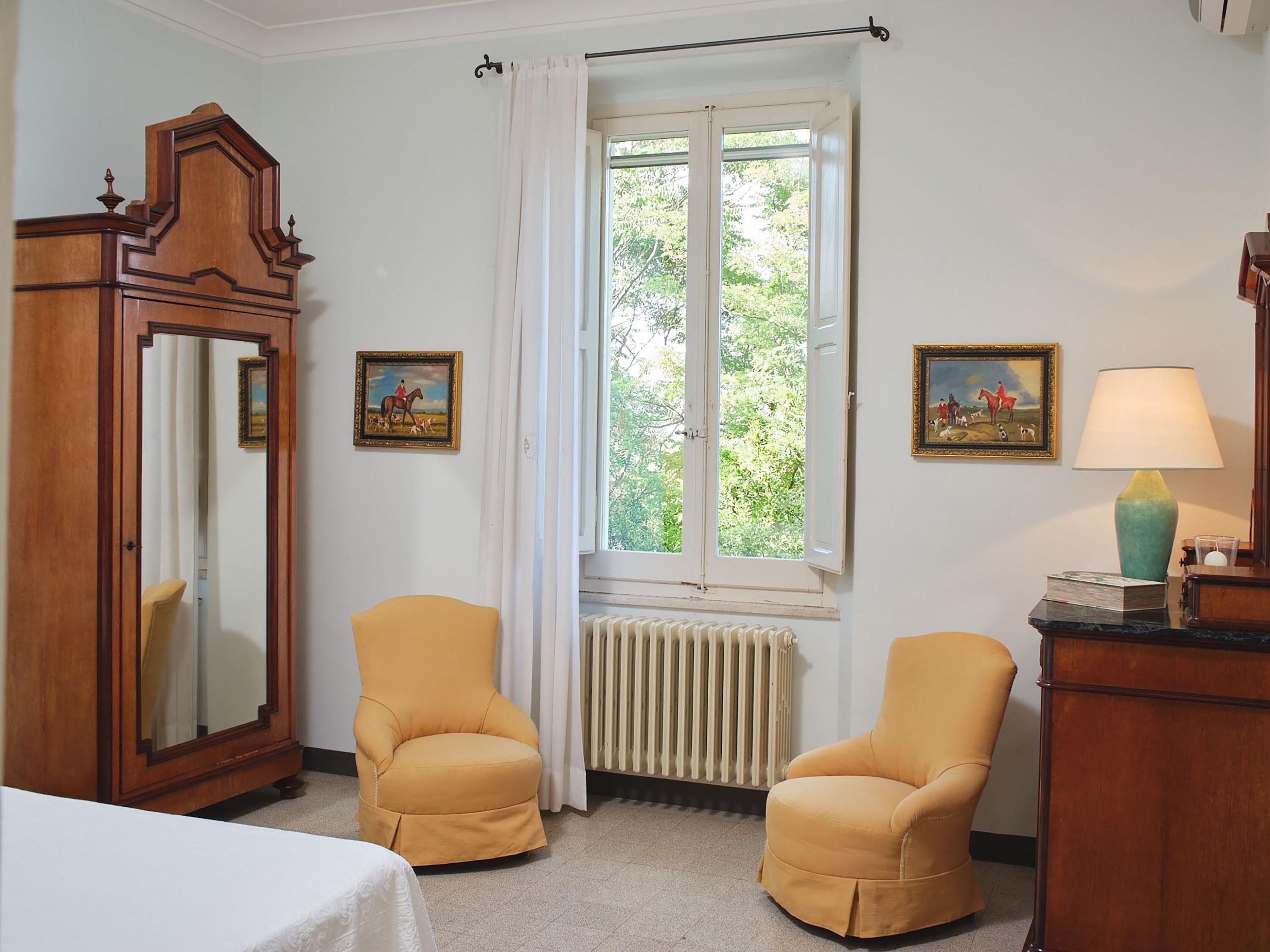 A room with two yellow armchairs, a wooden cabinet, a mirror, and a window with curtains.