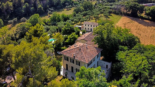 Une grande villa dotée d’un toit en tuiles, entourée d’une végétation luxuriante et agrémentée d’une piscine.