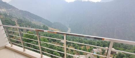 A balcony with a metal railing overlooking a valley with mountains in the background.