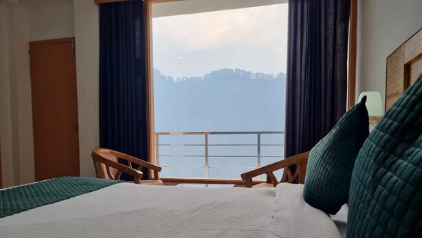 Habitación de hotel con una cama grande, dos sillas de madera, vista a un lago y montañas, y un cabecero de madera.
