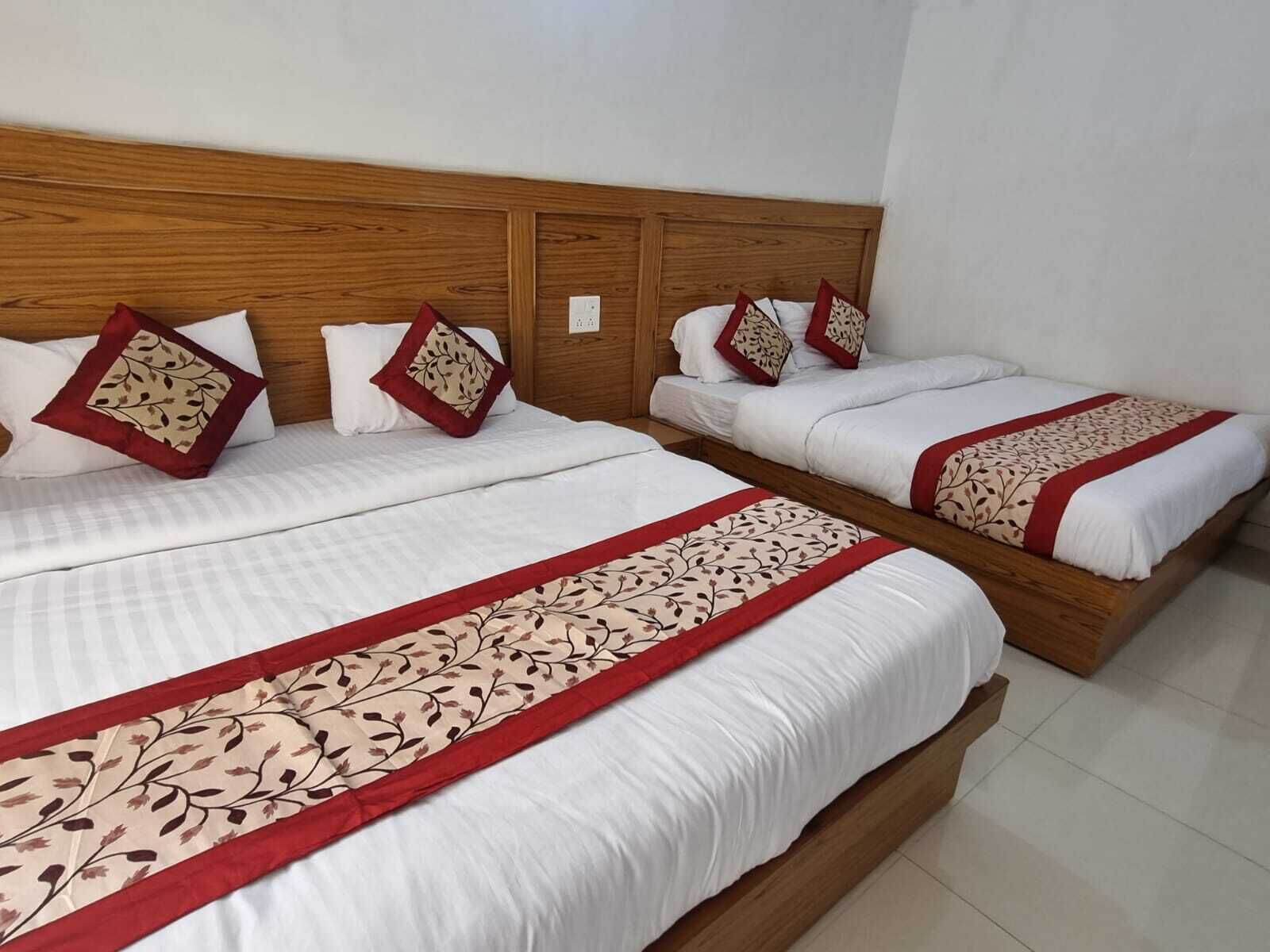 A hotel room with two beds, each with white bedding and red and beige decorative pillows.