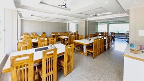 Un comedor amplio con varias mesas y sillas de madera, ventiladores de techo y ventanas grandes que ofrecen luz natural.