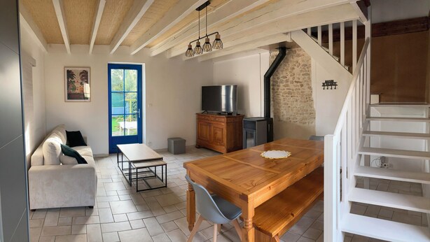 A cozy living room with a wooden dining table, a sofa, a TV, and a staircase. - Cottage for 4 to 6 persons + private jacuzzi (Péault)