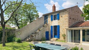 A stone house with blue shutters, a staircase leading to a second floor, and a patio with a table and chairs. - Cottage for 4 to 6 persons + private jacuzzi (Péault)