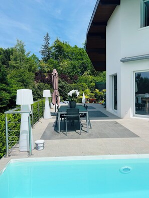 A modern outdoor patio with a pool, a dining table with chairs, and a covered umbrella. - Price drop magnificent villa in a quiet area with swimming pool and lake view (Annecy)