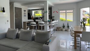 Un salon moderne avec un canapé, un coin repas comprenant une table et des chaises, et une cuisine en arrière-plan.