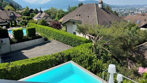 Un quartier résidentiel doté d’une piscine, entouré de haies et d’arbres bien entretenus, offrant une vue sur les montagnes lointaines et sur le paysage urbain.