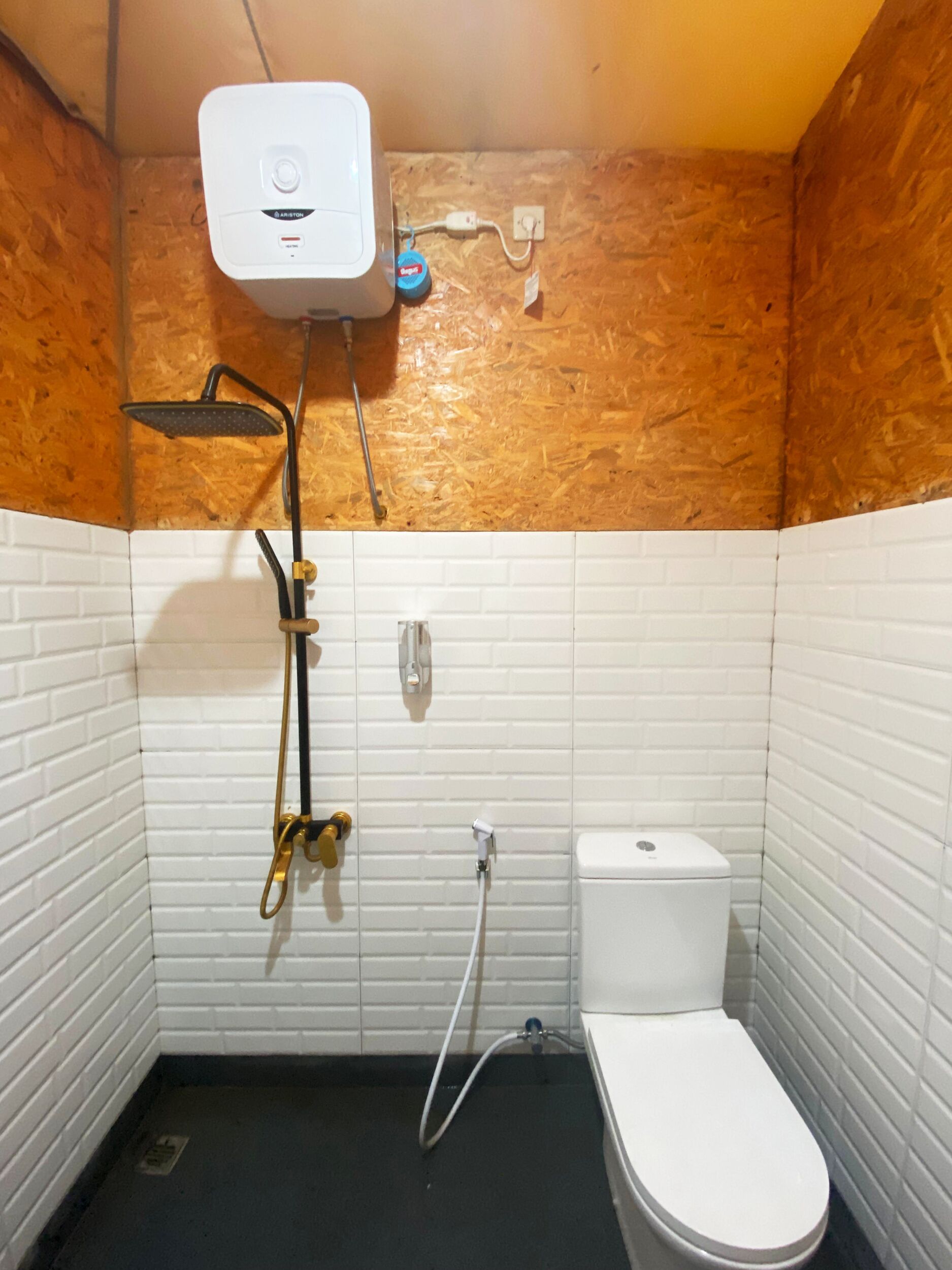 A small, compact bathroom with a white toilet, a shower with a handheld showerhead, and a water heater mounted on the wall.
