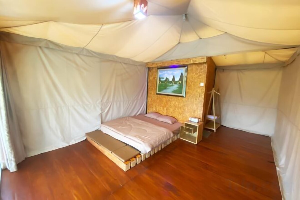 A tent with a bed, a small table, and a wall-mounted picture.