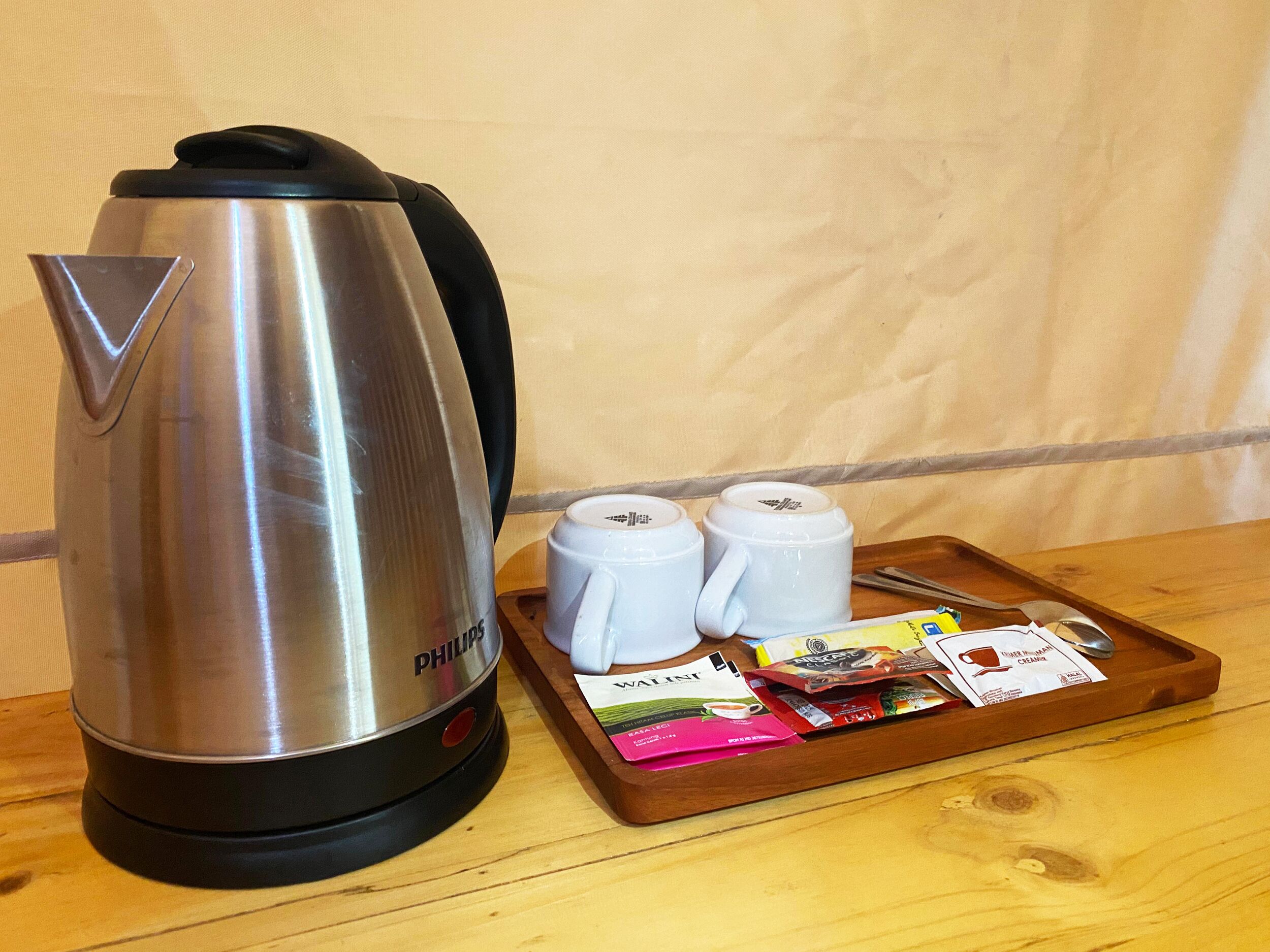 A stainless steel coffee maker with two white mugs and a tray with coffee pods.
