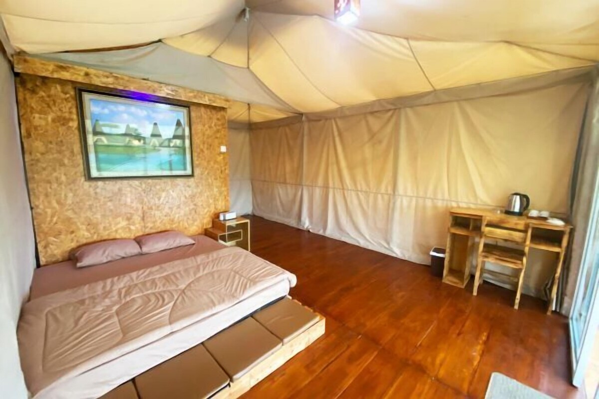 Een tent met een bed, een bureau en een ingelijst beeld aan de muur.