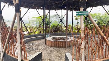 A covered outdoor area with a circular seating arrangement, bamboo structures, and a sign indicating an 'api ungun area'.