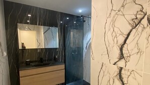 Ein modernes Badezimmer mit Marmor-Waschtisch, einer Duschkabine aus Glas und einem großen Spiegel.