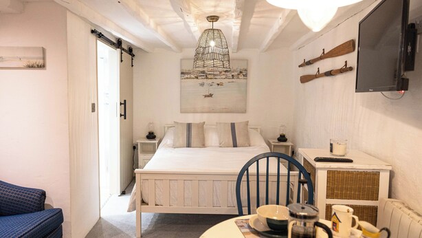 Ein Schlafzimmer mit einem Bett, einem Tisch mit Wasserkocher, einem Stuhl und einem Fernseher an der Wand.