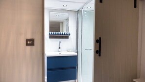 Ein modernes Badezimmer mit Duschkabine aus Glas, einem weißen Waschbecken und einem gestreiften Handtuch sowie einem blauen Schrank.