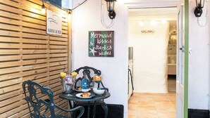 Eine Holzwand mit dem Schild "Sardine de Mer". Vor der Wand steht ein Tisch mit Stühlen und einem Schild mit der Aufschrift "Meerjungfrauenküsse & Fischgenüsse".
