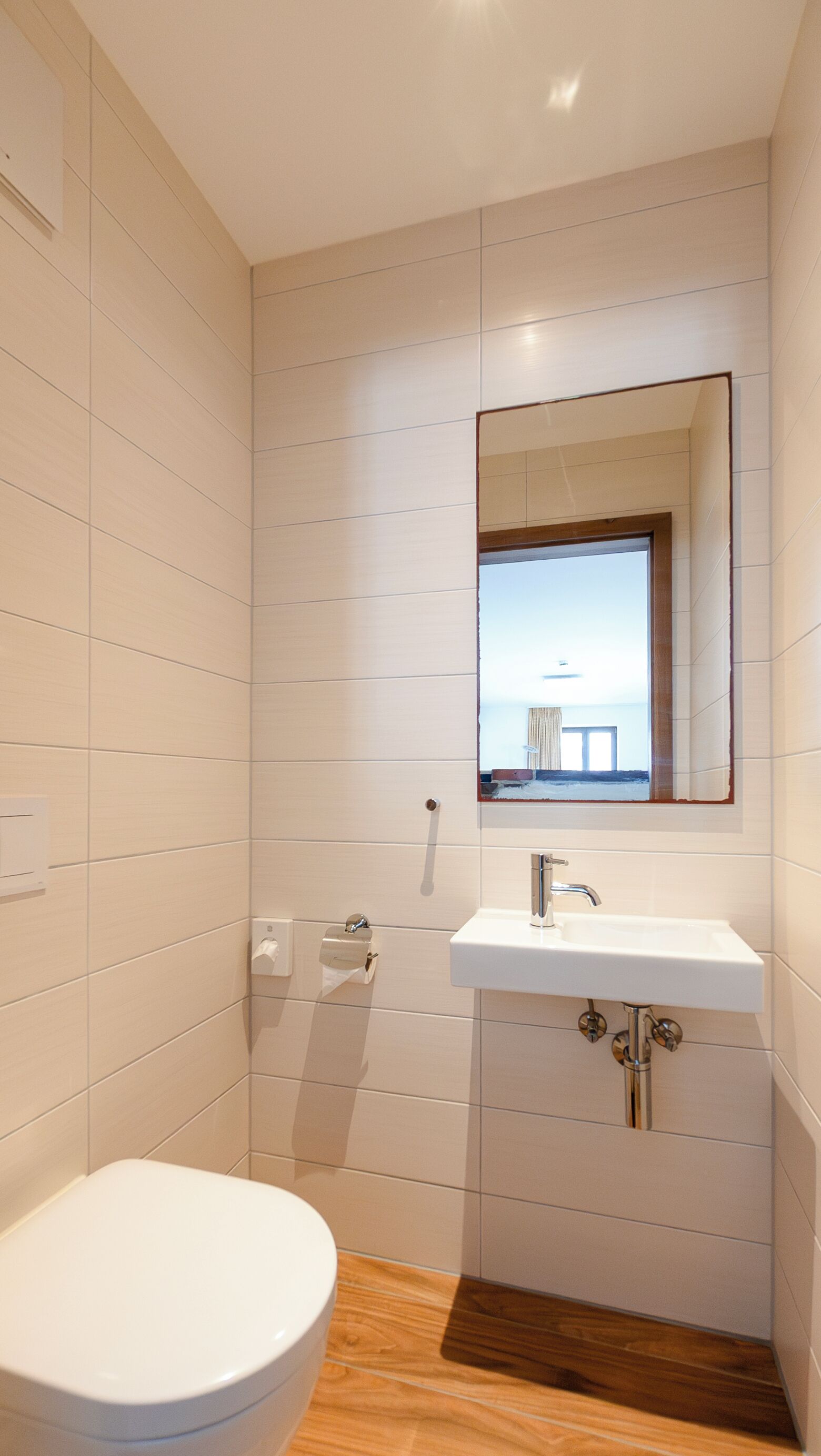 Un baño moderno con inodoro blanco, lavamanos con espejo y paredes con azulejos.