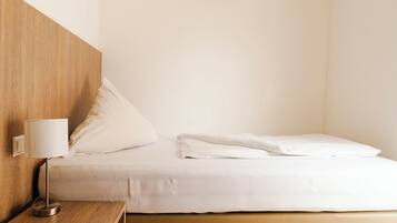 Una cama bien hecha con sábanas blancas, una mesita de noche con lámpara y un cabecero de madera.