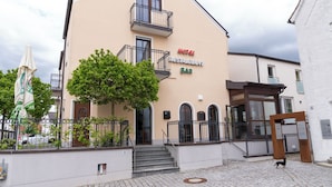 A hotel with a bar and restaurant, featuring a staircase leading to the entrance, a tree in front, and a dog on the pavement. - Henrys Sleeping Buttenwiesen (Buttenwiesen)