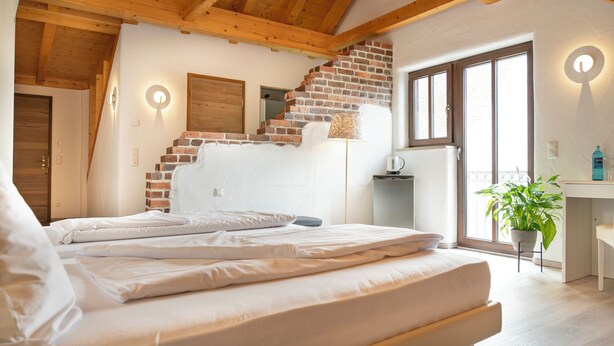 A bedroom with a brick wall, a bed, a desk, and a window with a view. - Henrys Sleeping Buttenwiesen (Buttenwiesen)