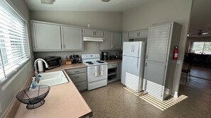 Una cocina compacta con gabinetes blancos, estufa, microondas, refrigerador y lavamanos.