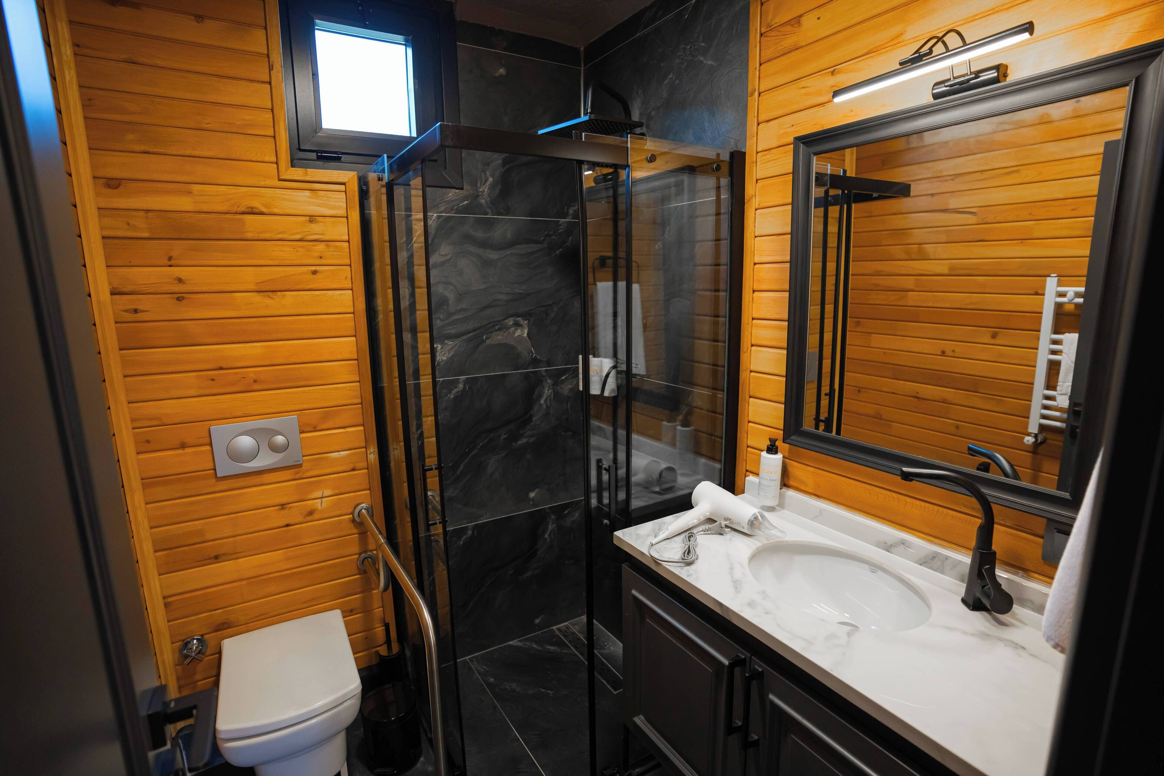 A modern bathroom with a glass shower enclosure, wooden walls, a white sink, and a large mirror.