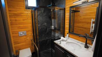 A modern bathroom with a glass shower enclosure, wooden walls, a white sink, and a large mirror.