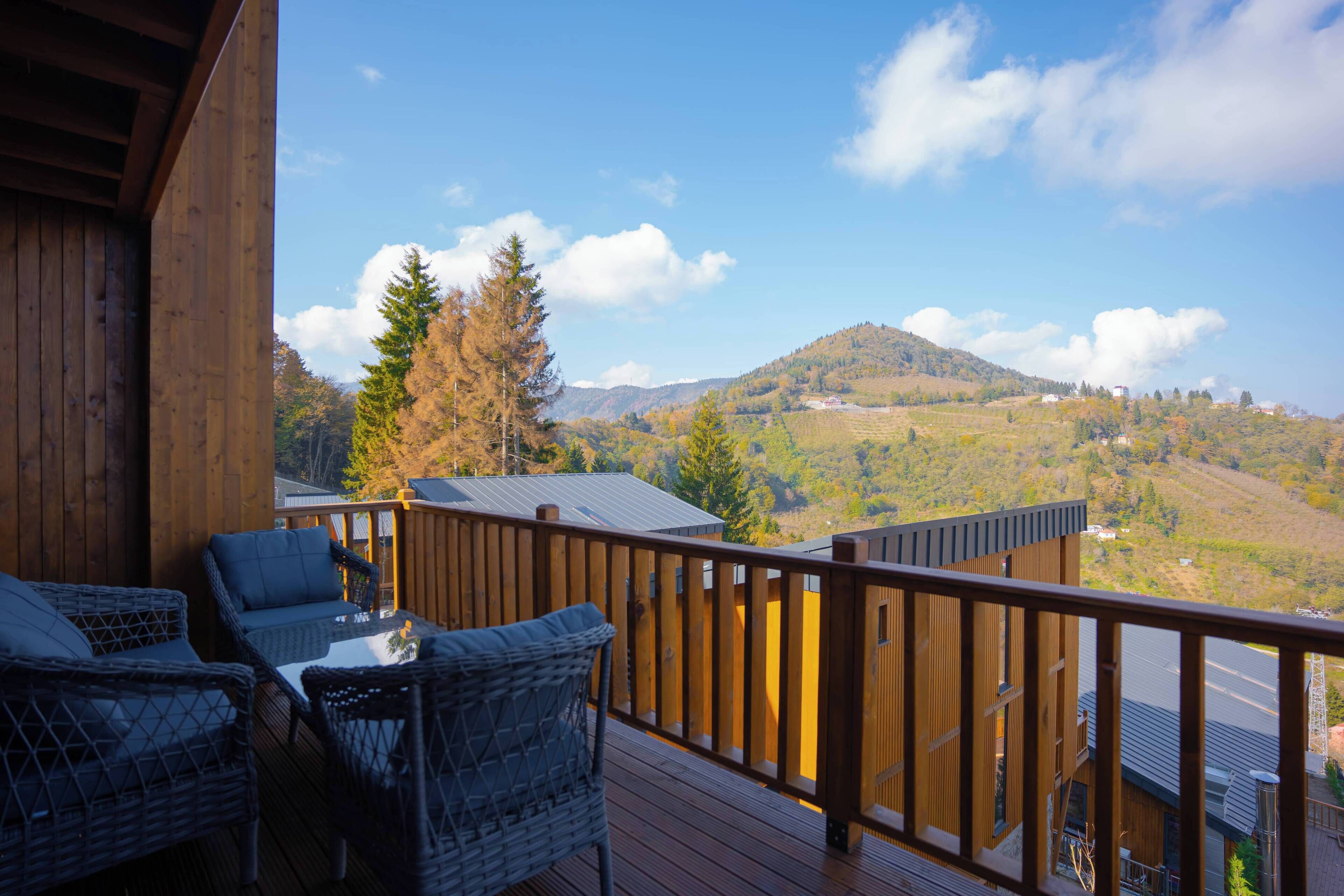 A wooden deck with wicker furniture and a view of a hilly landscape.