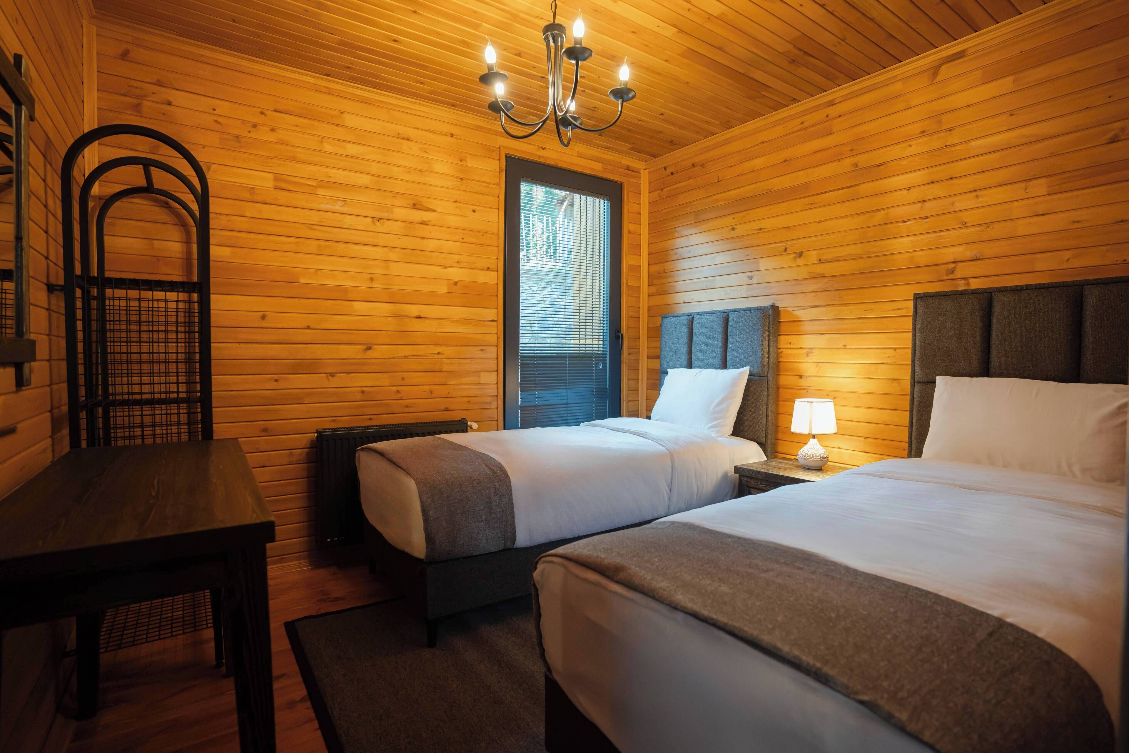 Une pièce de style cabane en bois, comprenant deux lits, une table, une chaise et un lustre.