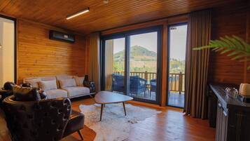 A wooden interior with a sofa, a leather chair, a table, and a view of a deck and hills.