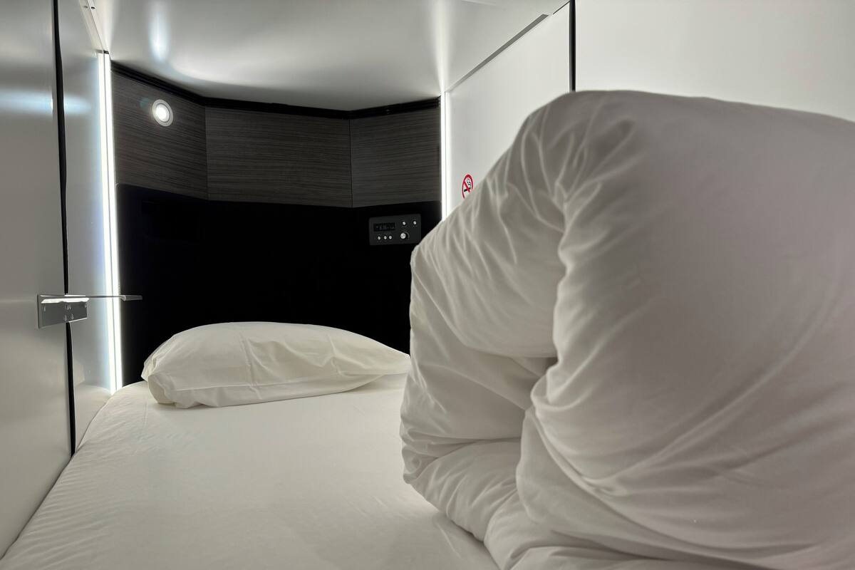 A modern hotel room with a neatly made bed, a control panel, and a door with a no-smoking sign.