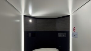 A compact, modern hotel room with a single bed, a control panel, and a no-smoking sign. - Capsulehotel Suzumoriya (Tokyo)