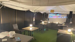 An indoor seating area with tables, chairs, and a projection screen displaying various channels. - Capsulehotel Suzumoriya (Tokyo)