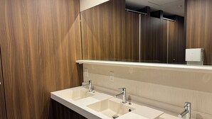 A modern bathroom with wooden paneling, a large mirror, and a double sink with chrome fixtures. - Capsulehotel Suzumoriya (Tokyo)