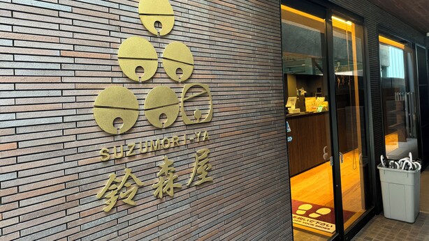 A brick wall with a logo and Japanese characters, indicating a commercial establishment. - Capsulehotel Suzumoriya (Tokyo)