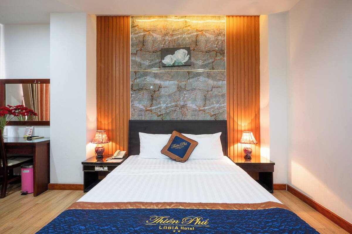 Une chambre d’hôtel avec un grand lit, une table de chevet avec une lampe, un miroir et un panneau décoratif mural.