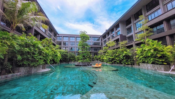 A modern hotel with a central swimming pool surrounded by lush greenery and multiple floors of balconies.