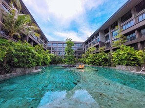 Un hotel moderno con una piscina central rodeada de abundante vegetación y múltiples balcones.