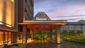 A modern hotel entrance with a covered walkway, a prominent sign reading "Oahu," and a landscaped garden area with palm trees.