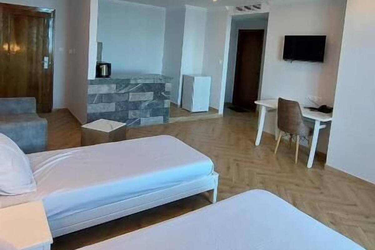 A modern hotel room with two beds, a small dining area, a TV, and a stone fireplace.